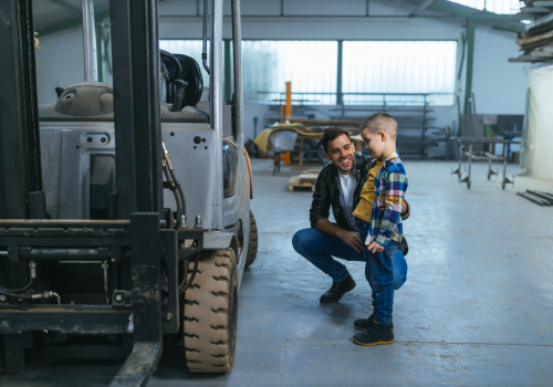 Man who works in warehouse showing to his son how to drive forklift